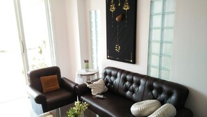 Una sala moderna con un sofá de cuero, una mesa de centro de vidrio y una obra de arte negra en la pared.