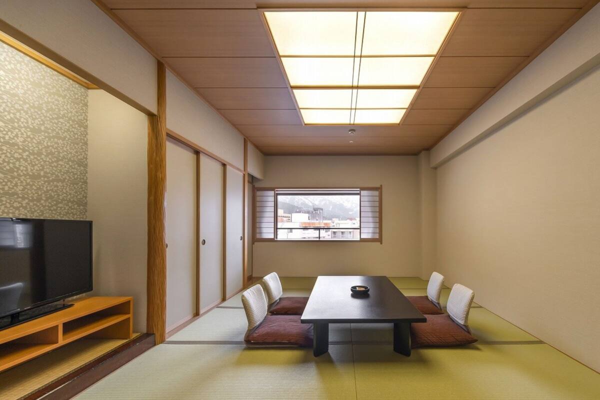 A traditional Japanese-style room with tatami flooring, a low table, and a television on a wooden stand.