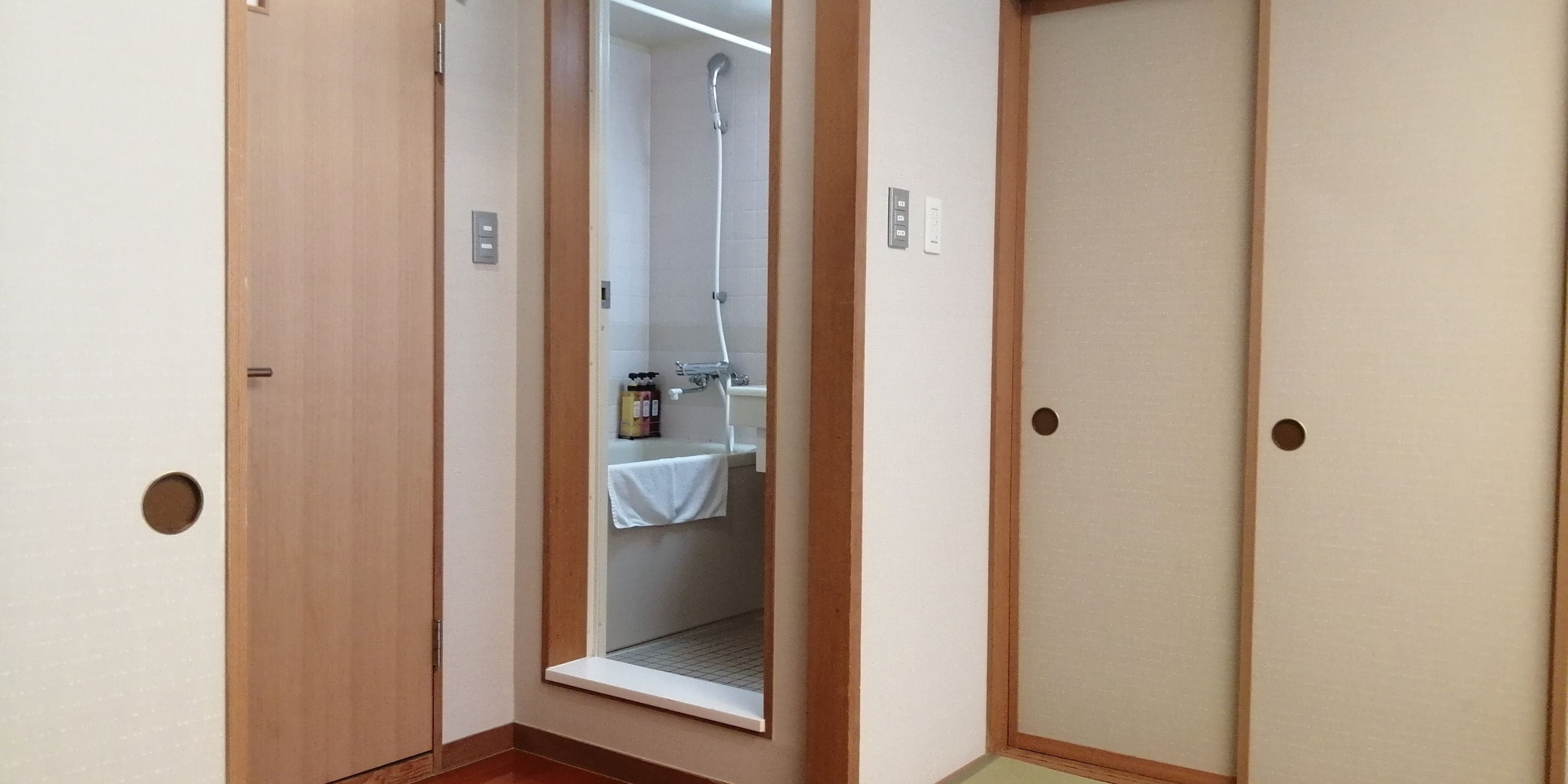 A narrow hallway with wooden doors and a visible shower area with a towel hanging on the wall.