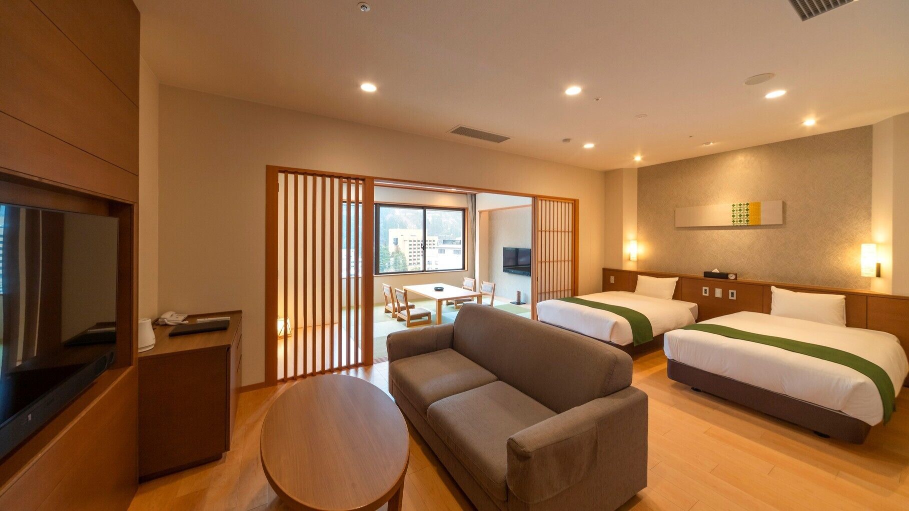 A hotel room with two beds, a sofa, a TV, a desk, and a sliding door leading to a balcony.