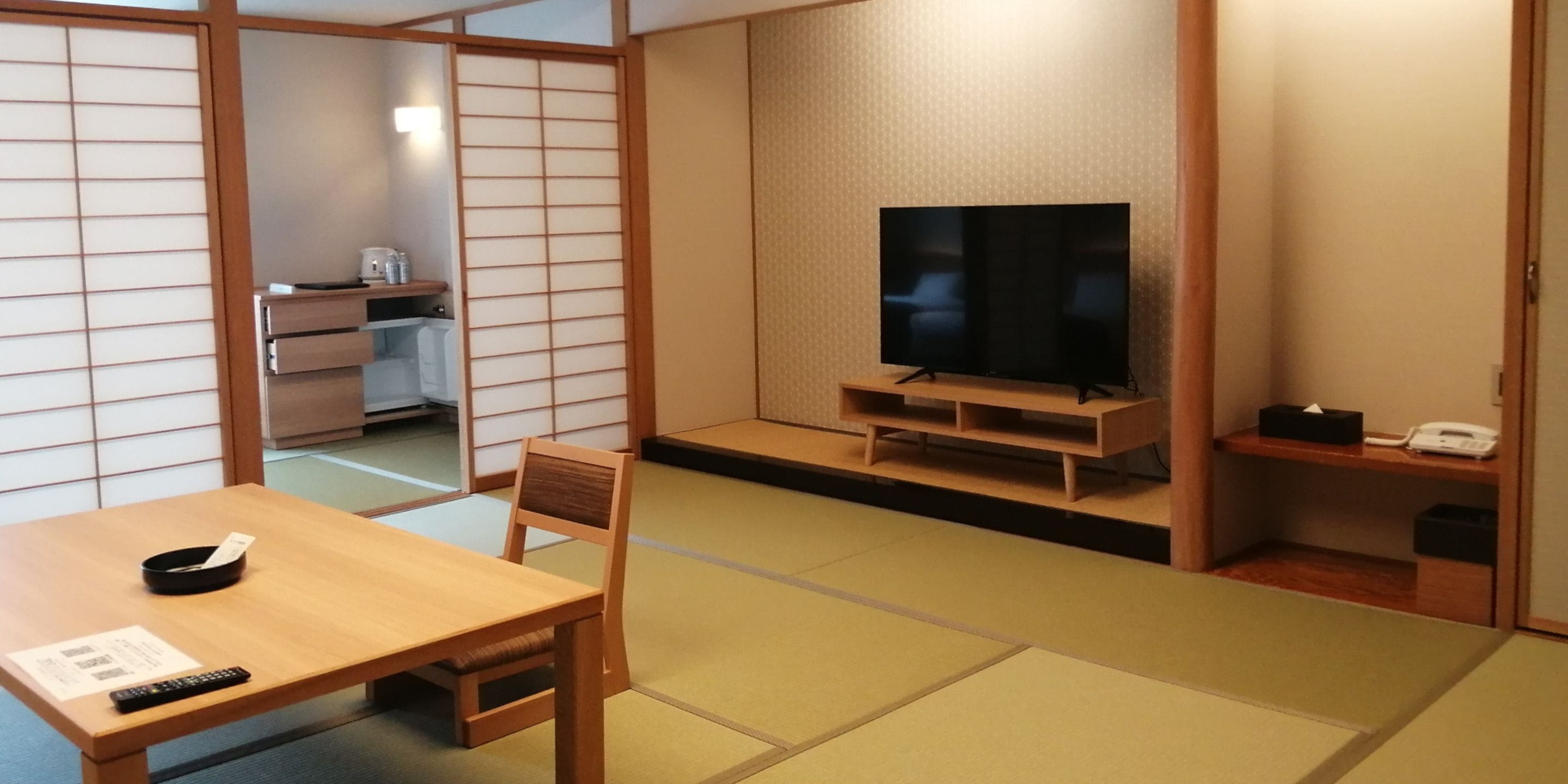 A traditional Japanese room with tatami flooring, a low wooden table, a television, and a sliding door.