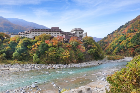 A hotel with multiple floors, a river in the foreground, and a mountainous backdrop. - Kurobe Unazuki Onsen Yamanoha(ORIX HOTELS & RESORTS) (Kurobe)
