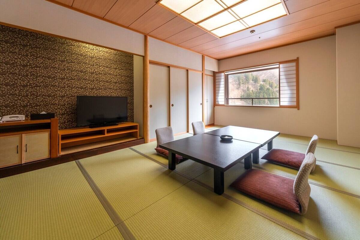 A traditional Japanese room with tatami flooring, a low table, cushions, a television, and a sliding door.
