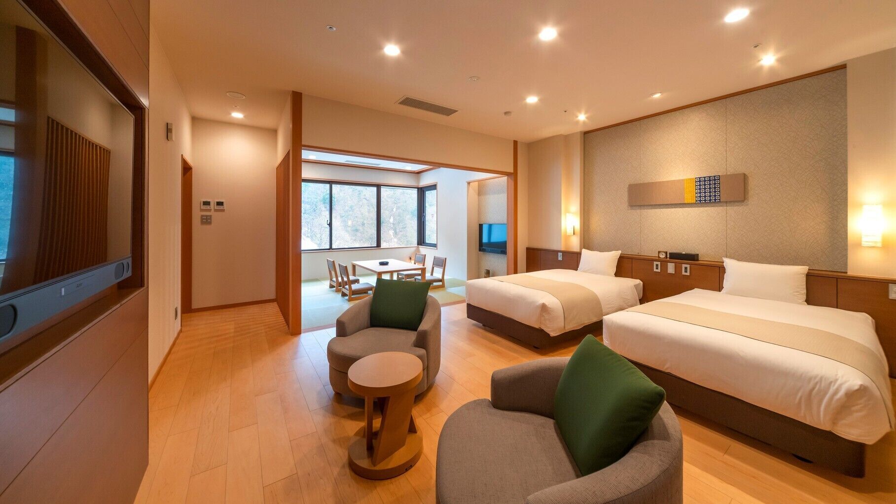 A hotel room with two beds, a TV, a dining area with a table and chairs, and a large window.