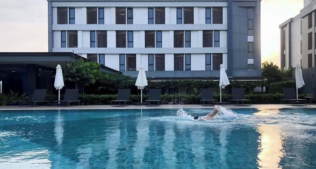 A swimming pool with lounge chairs and umbrellas, surrounded by a modern building with multiple floors and windows.