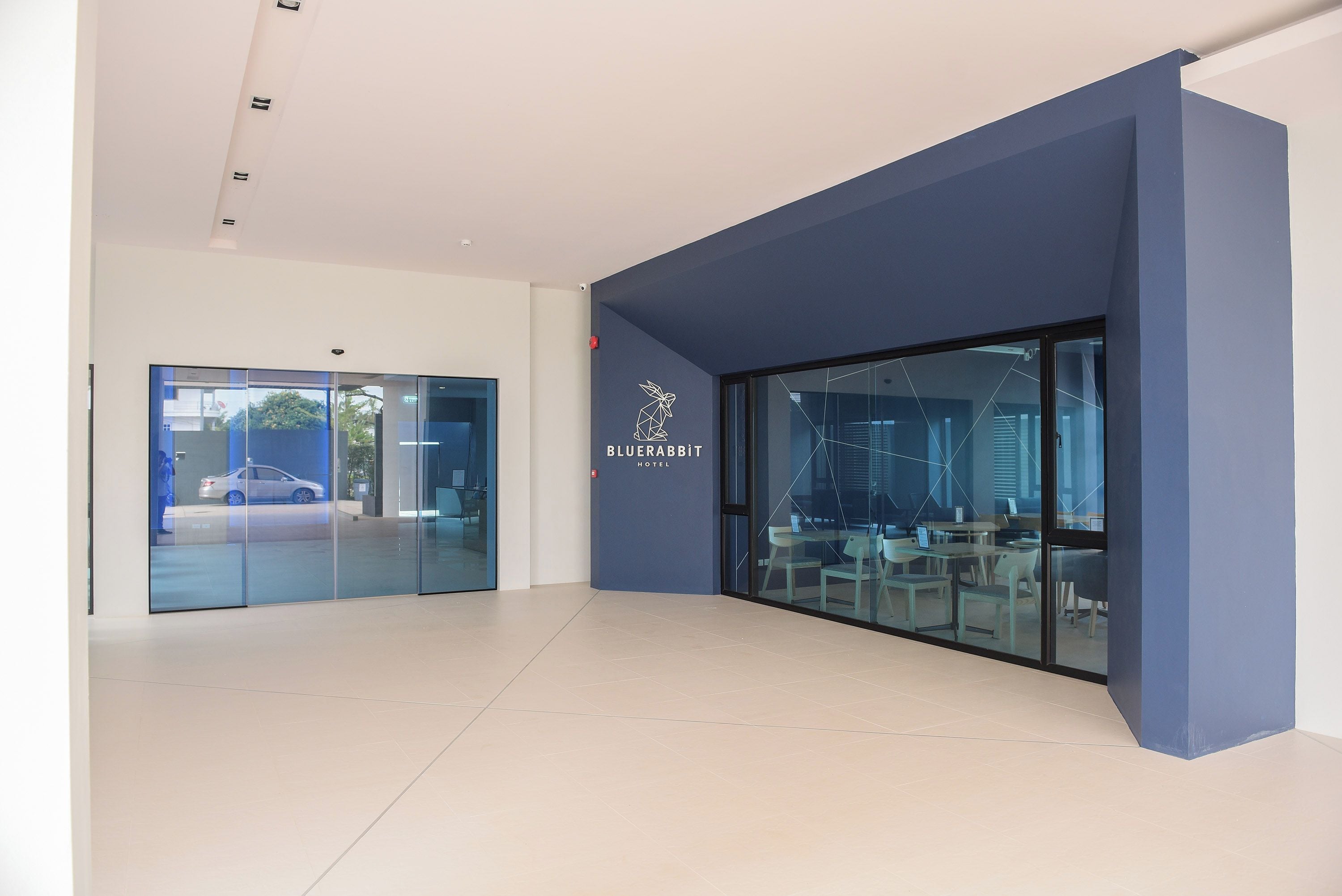 Un lobby moderno de hotel con entrada de vidrio, un logotipo en la pared y vistas al exterior.