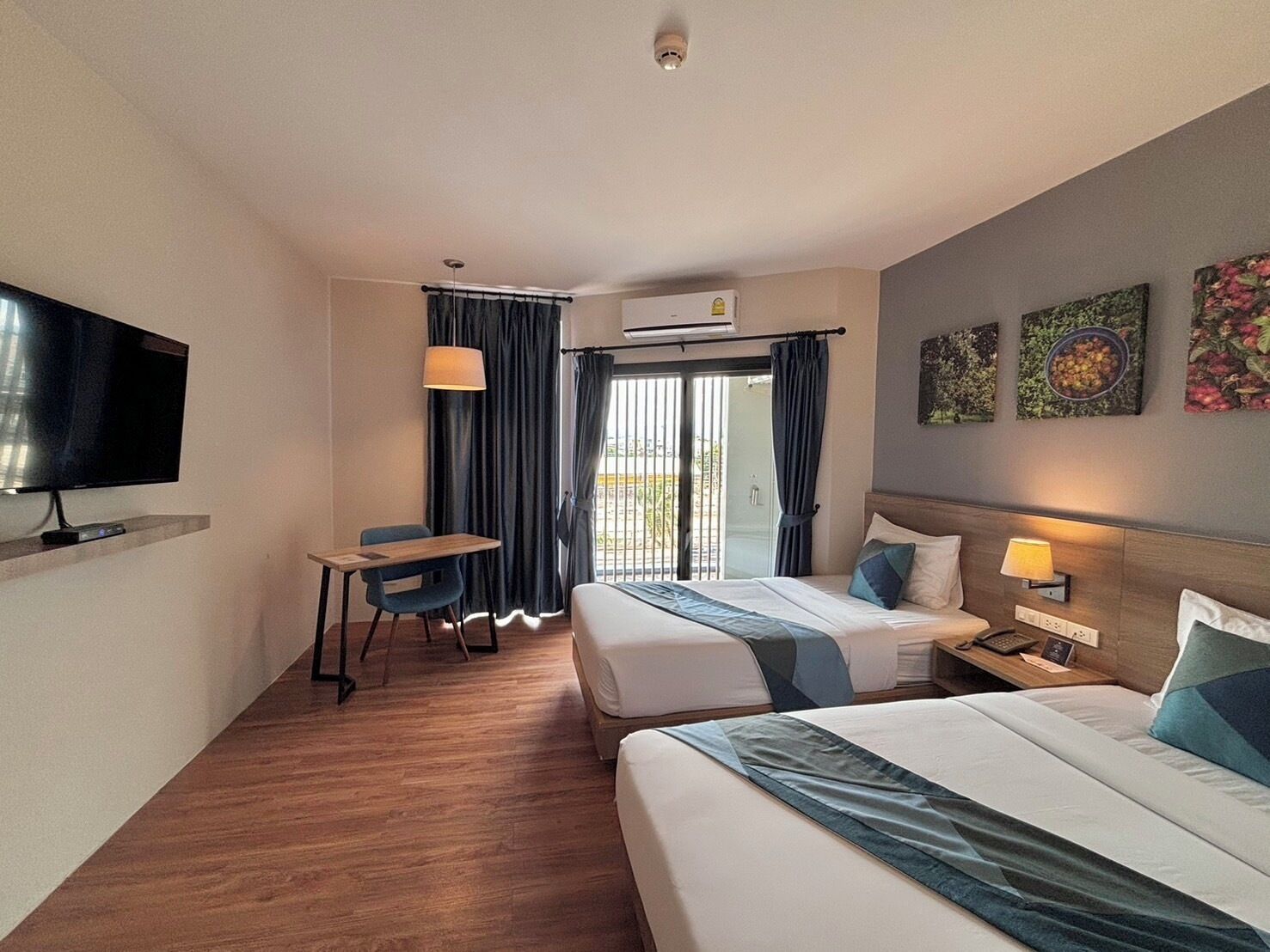 Habitación de hotel con cama, escritorio, televisor y balcón con cortinas.