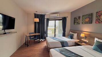 Habitación de hotel con cama, escritorio, televisor y balcón con cortinas.