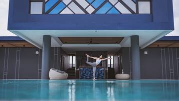 Un edificio moderno con zona de piscina, mostrando a una persona practicando una postura de yoga.