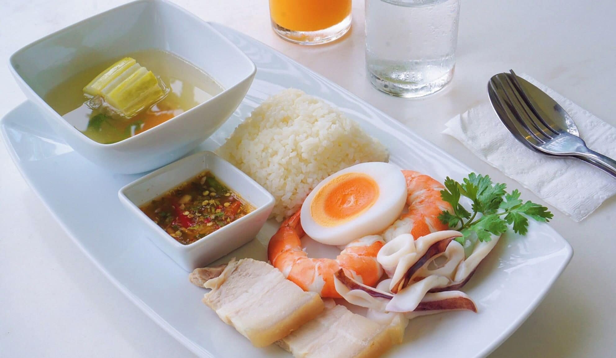 A meal consisting of rice, a boiled egg, a piece of fish, and a bowl of soup with vegetables.