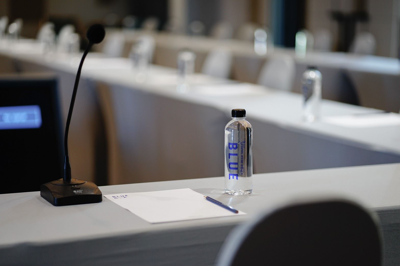 Una mesa de conferencias con un micrófono, una botella etiquetada 'BLUE' y un bloc de notas.