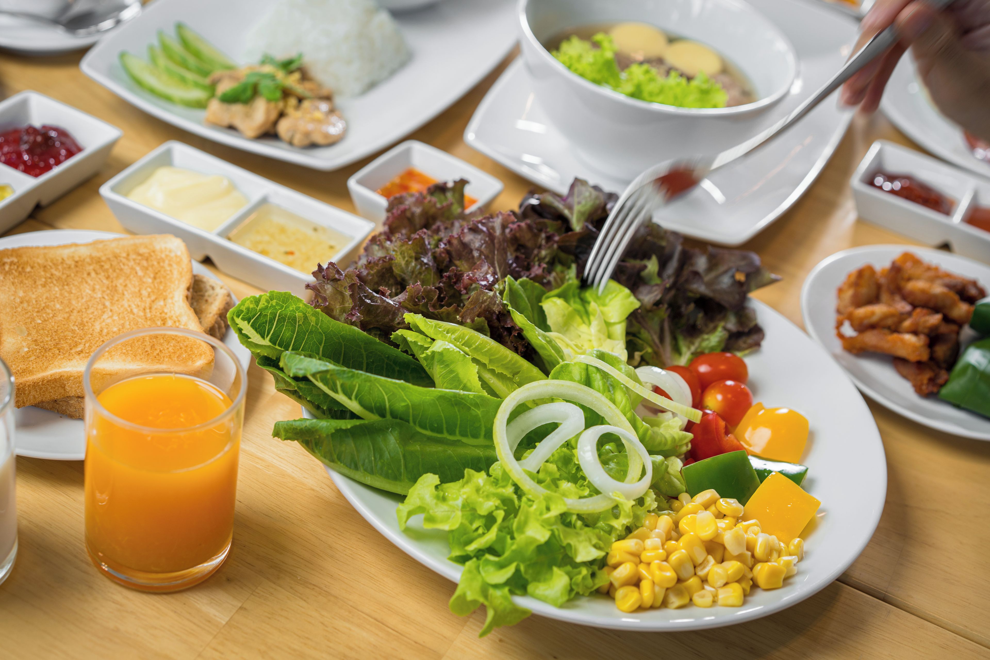 A breakfast setting with various dishes including toast, salad, and a glass of orange juice.