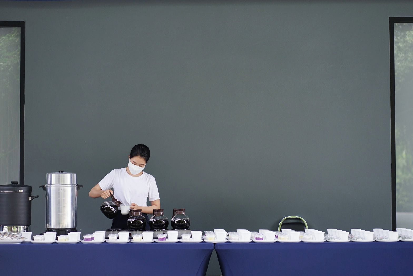 A person serving tea from a teapot at a table with multiple teacups and a kettle.