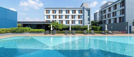 Un hotel moderno con piscina, sillas de descanso y un jardín bien cuidado.