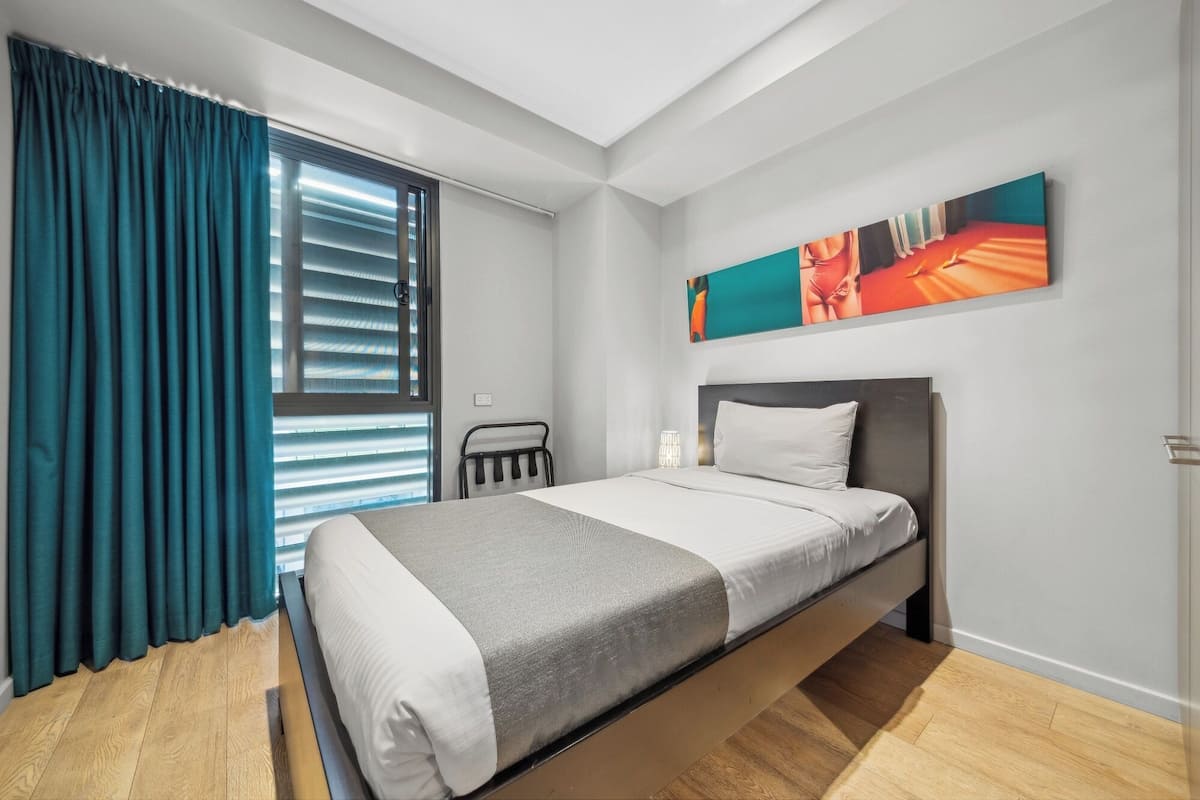 A modern bedroom with a bed, a window with curtains, a headboard, and a wall-mounted artwork.