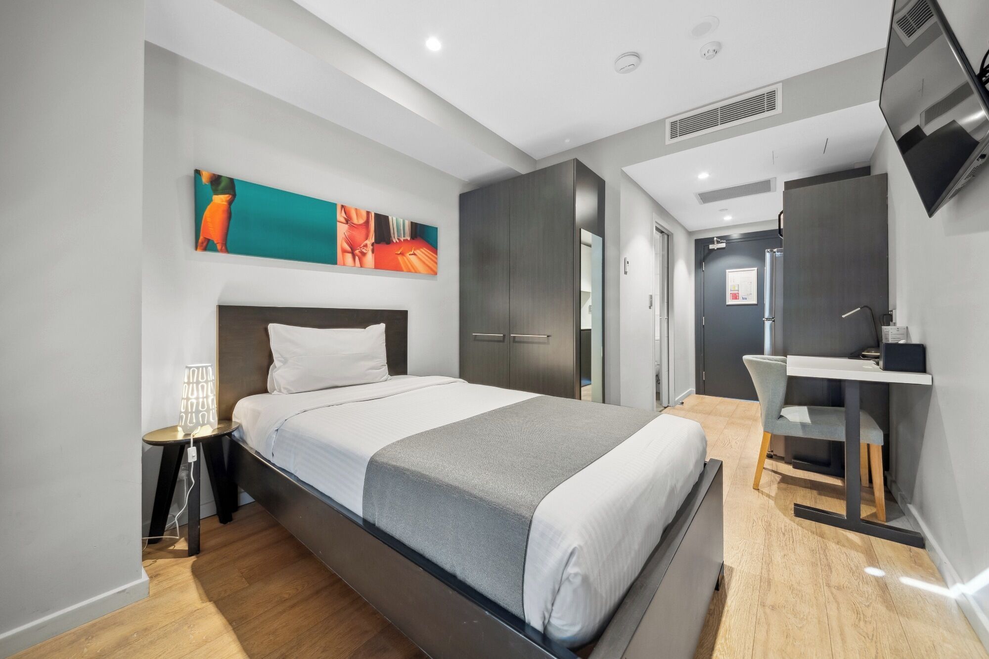 A modern hotel room with a large bed, a desk, and a TV.