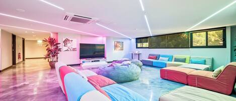 A modern living room with a large flat-screen TV, colorful bean bags, and a sofa set.