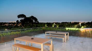 Une terrasse extérieure avec trois tables et des bancs en bois, entourée d’une rambarde en verre.