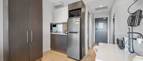 Una cocina moderna con armarios de madera oscura, un refrigerador de acero inoxidable y un microondas. Hay una encimera blanca con un teléfono y una taza.