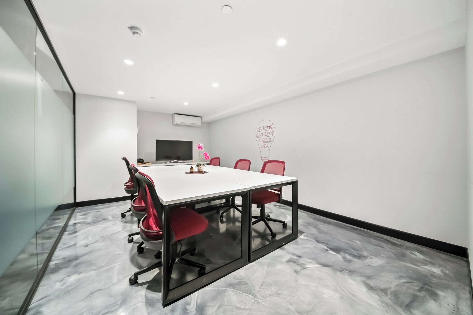A conference room with a white table, red chairs, a flat-screen TV, and a motivational wall art.