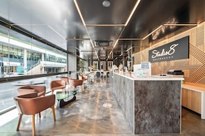 A modern interior with a reception desk, seating area, and large windows overlooking a street. - Studio 8 Residences in Ryde (Ryde)