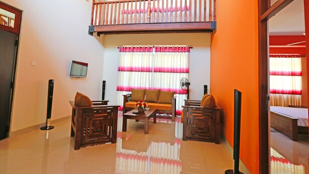 A spacious living area with a high ceiling, a balcony with wooden railings, a sofa set, and a television mounted on the wall. - APL Apartments (Peliyagoda)