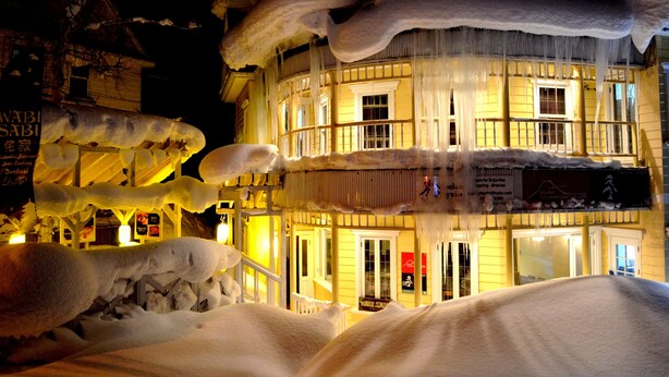 A building with a yellow facade and multiple windows, surrounded by snow and icicles. - Australia House (Kutchan)