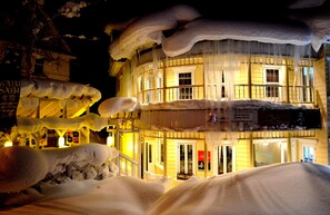 A building with a yellow facade and multiple windows, surrounded by snow and icicles.