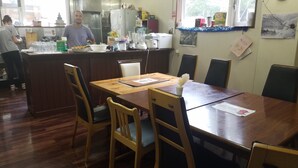 A dining area with a wooden table and chairs, a kitchen in the background, and a window with a view. - Australia House (Kutchan)