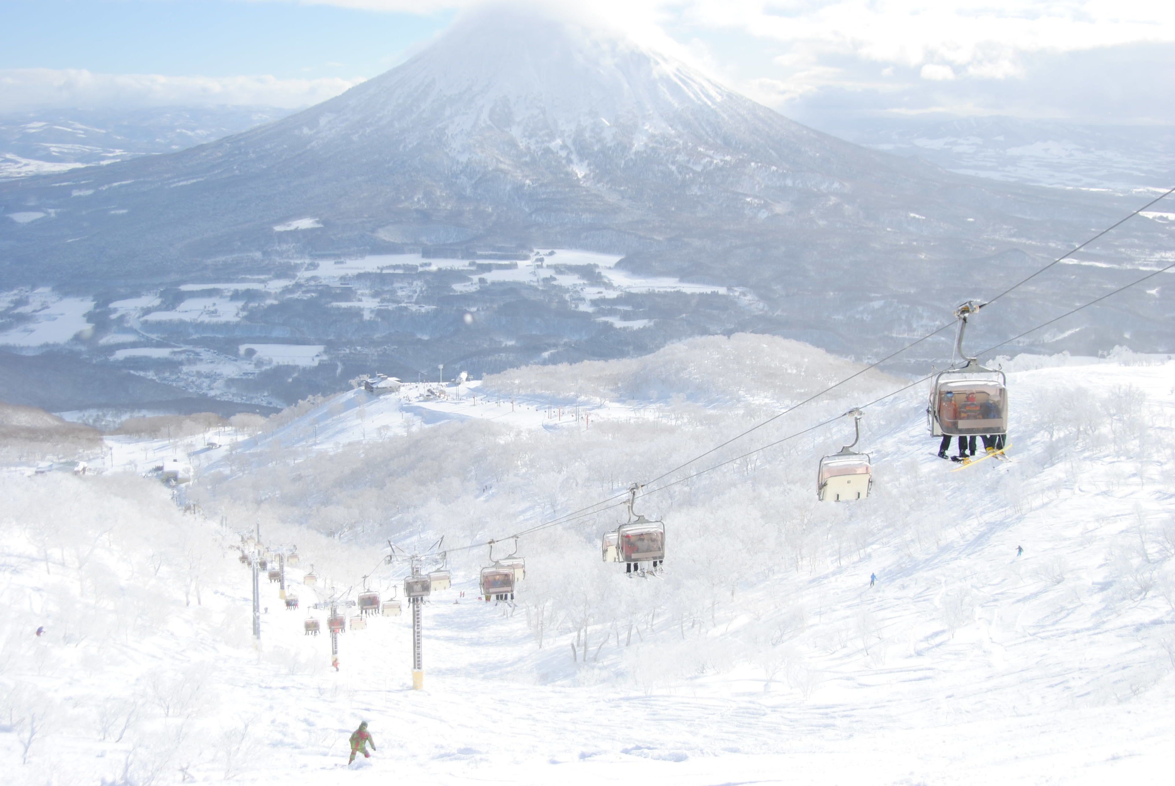 A ski lift with cabins ascending a snowy slope, a mountain in the background, and a clear sky.