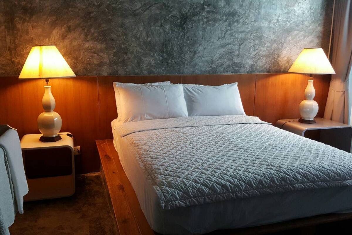 A hotel room with a large bed, two bedside lamps, a wooden headboard, and a textured wall.