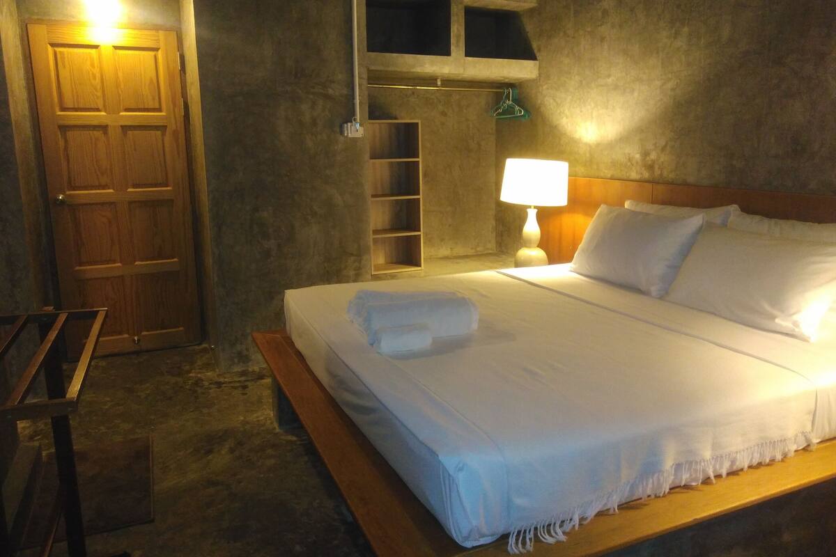 A neatly made bed with white linens, a bedside lamp, and a wooden headboard.