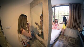 A hotel room with a large mirror, a bed, a window with curtains, and a tiled floor.