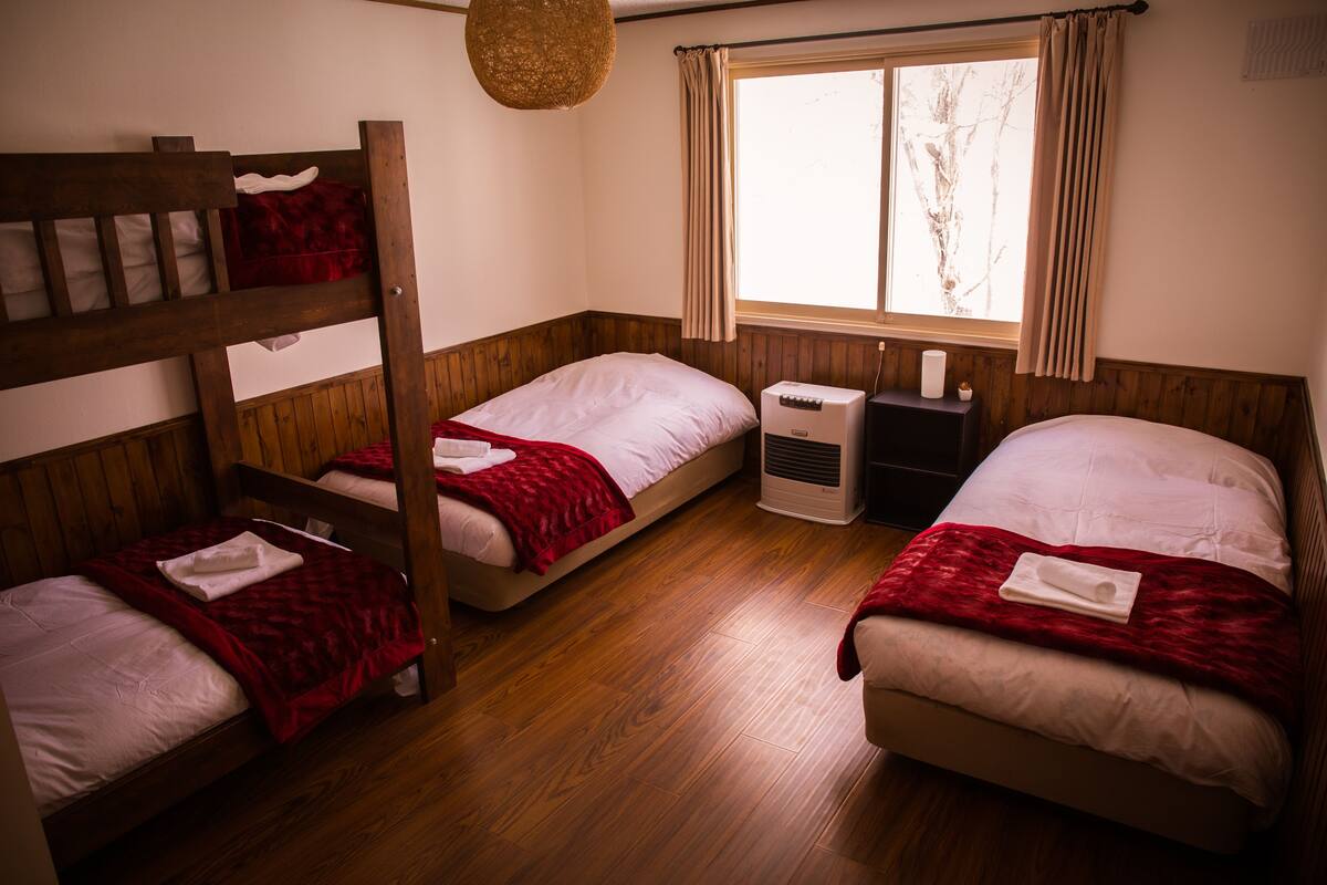 Habitación con tres camas, piso de madera, una ventana con cortinas y una lámpara colgante.