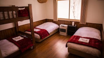 A room with three beds, wooden flooring, a window with curtains, and a hanging light fixture.