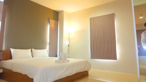 A hotel room with a large bed, a bedside table, a lamp, and a window with curtains. - The Pride (Sam Phran)