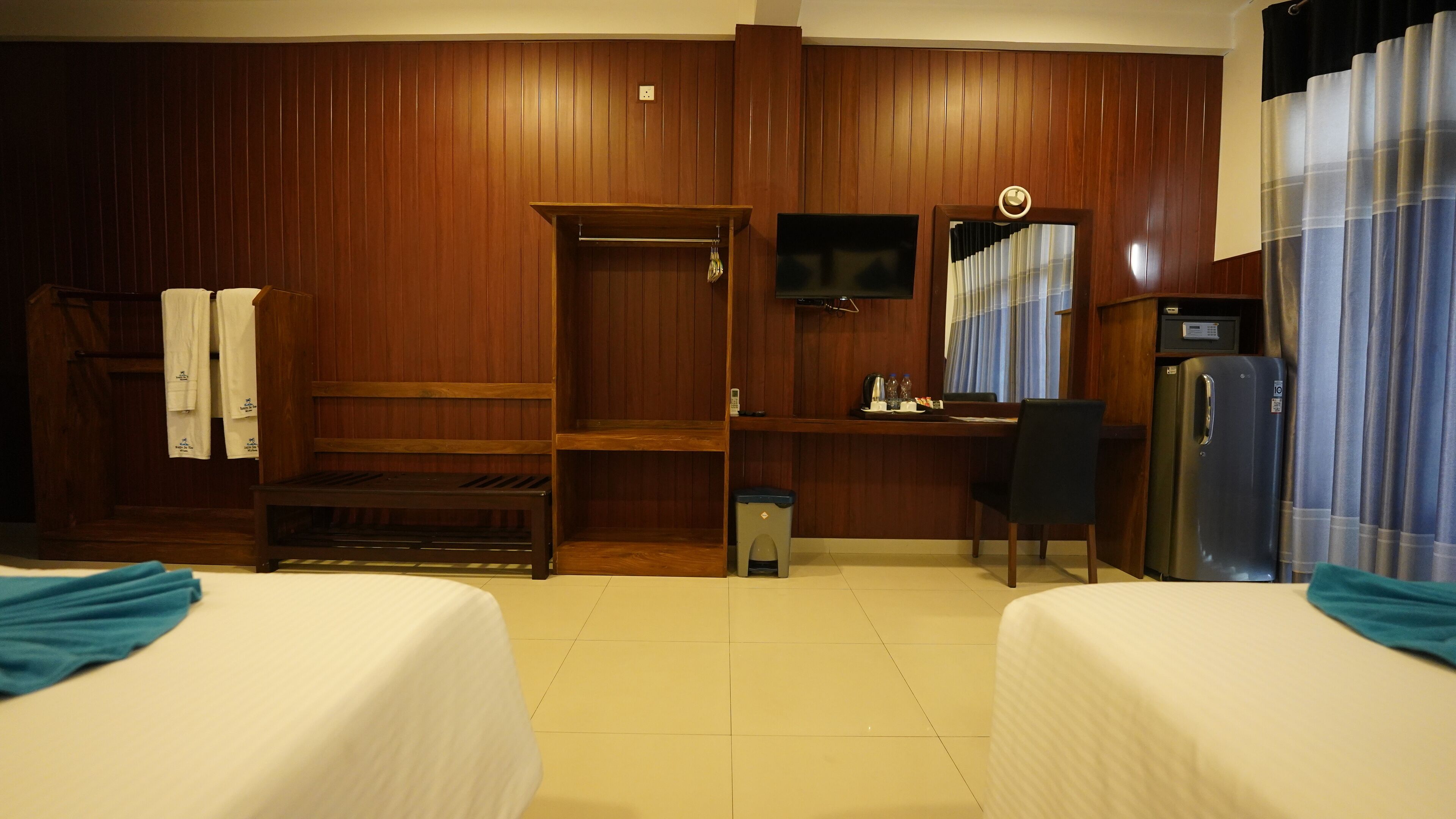 Ein Hotelzimmer mit Holzwänden, einem Schreibtisch mit Stuhl, einem Fernseher, einem Kühlschrank und zwei Betten.