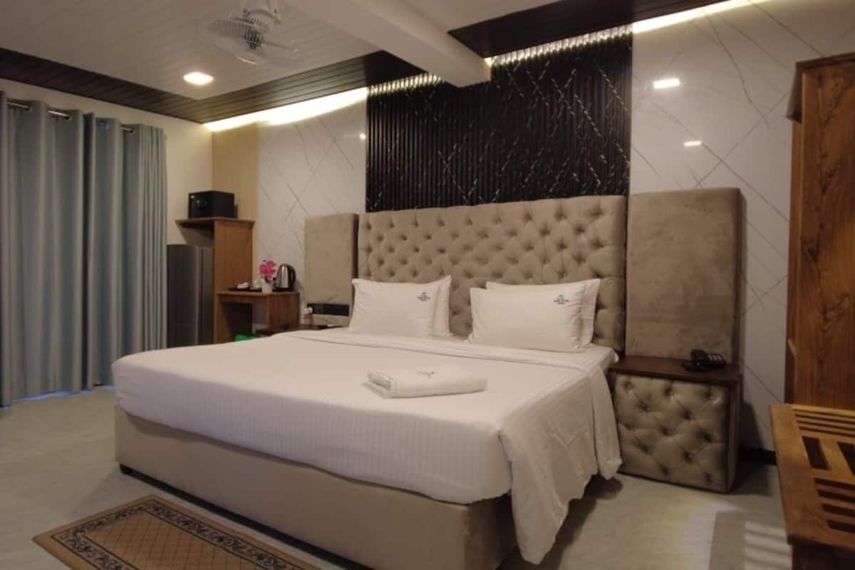 A hotel room with a large bed, a desk, a chair, and a wardrobe.