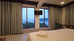Ein Hotelzimmer mit Bett, Fernseher, Sessel und Blick auf ein Gewässer.