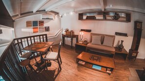 Una sala acogedora con una mesa de comedor de madera, sofá y una mesa de centro. Se ve una escalera que sube a un nivel superior, y un estante de pared con objetos decorativos.