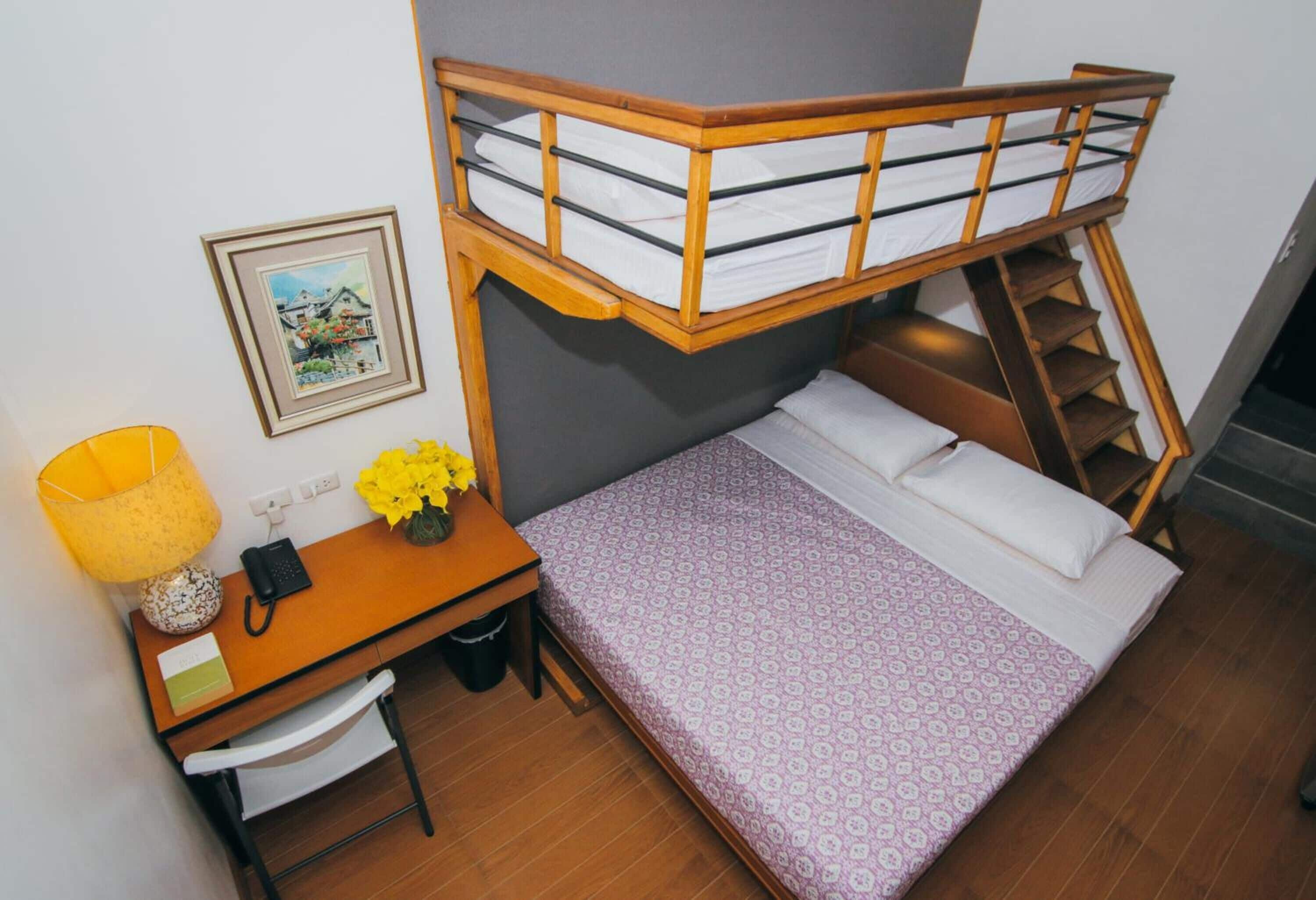 A bunk bed with a desk, chair, and a small table with a lamp and flowers.