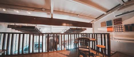 A wooden-floored interior with a staircase leading to an upper level, a dining area with chairs and stools, and a wall with patterned artwork.