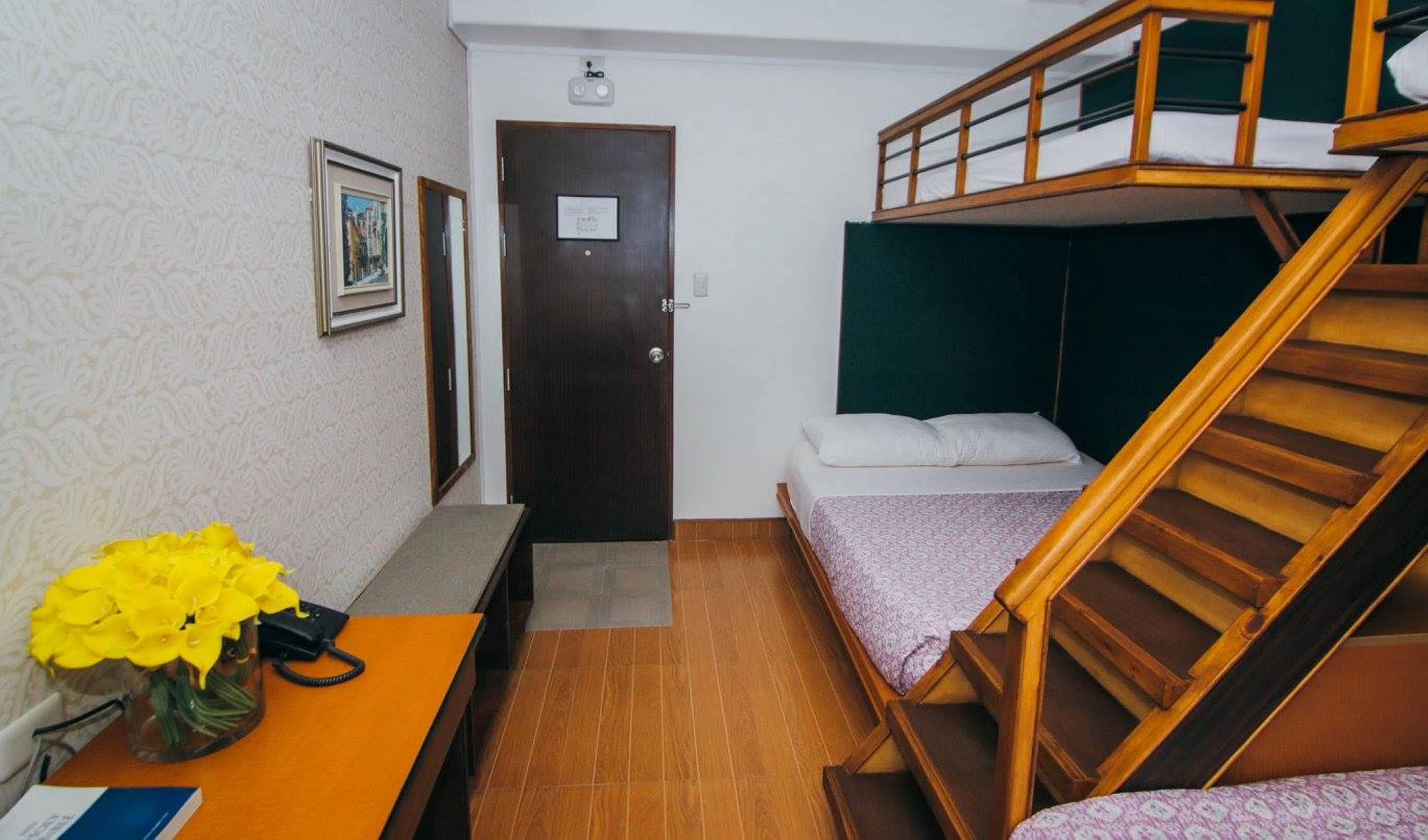 A compact room with a bunk bed, a desk with a vase of flowers, and a door with a sign.
