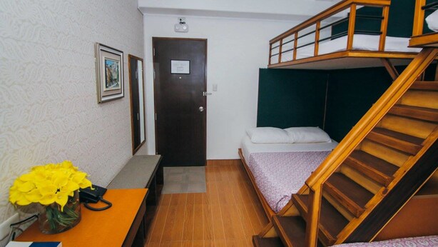 A compact room with a bunk bed, a desk with a vase of flowers, and a door with a sign. - Amaris Bed & Breakfast (Lapu-Lapu)