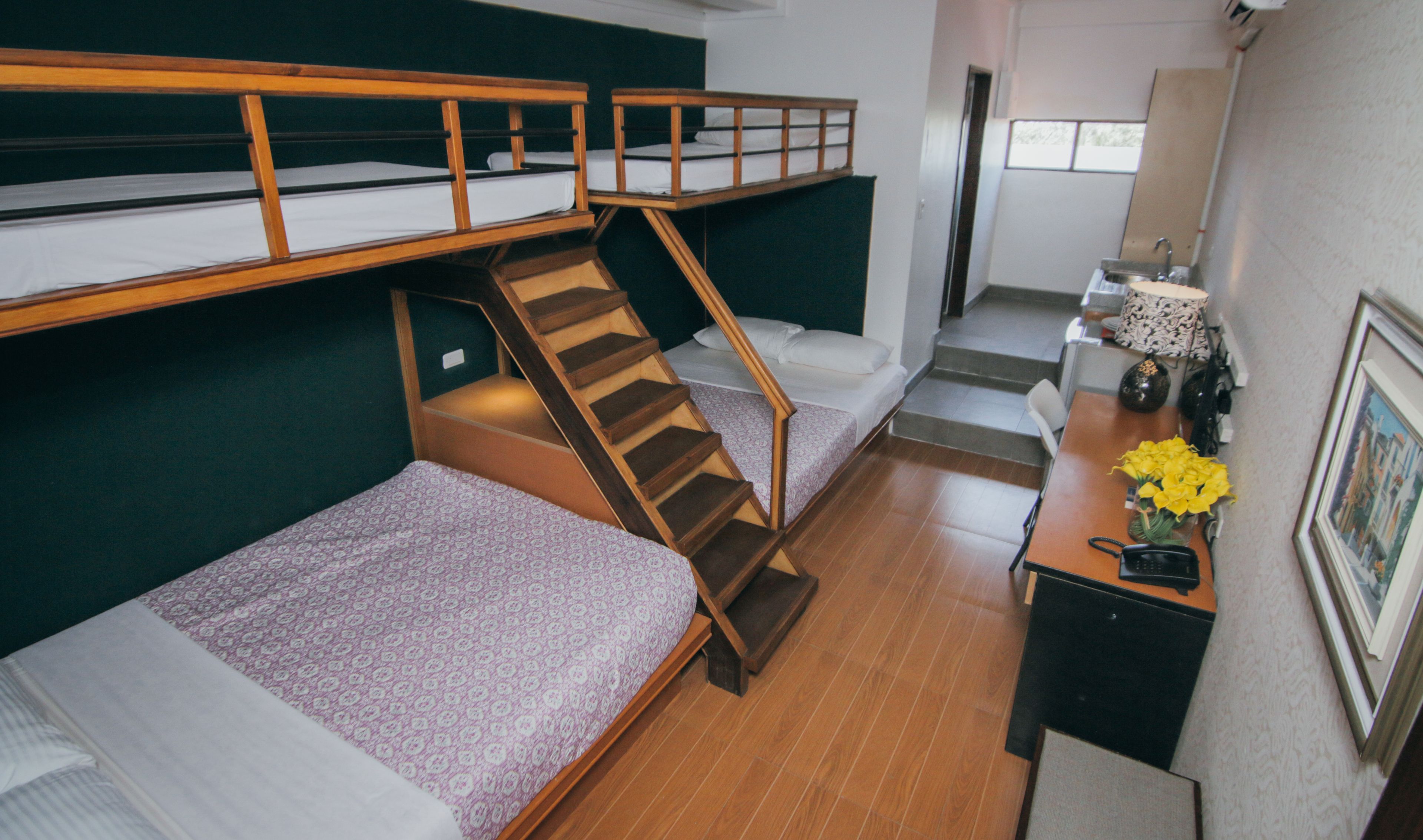 Um quarto em dormitório com beliches, uma escrivaninha, uma cadeira e um lance de escadas.