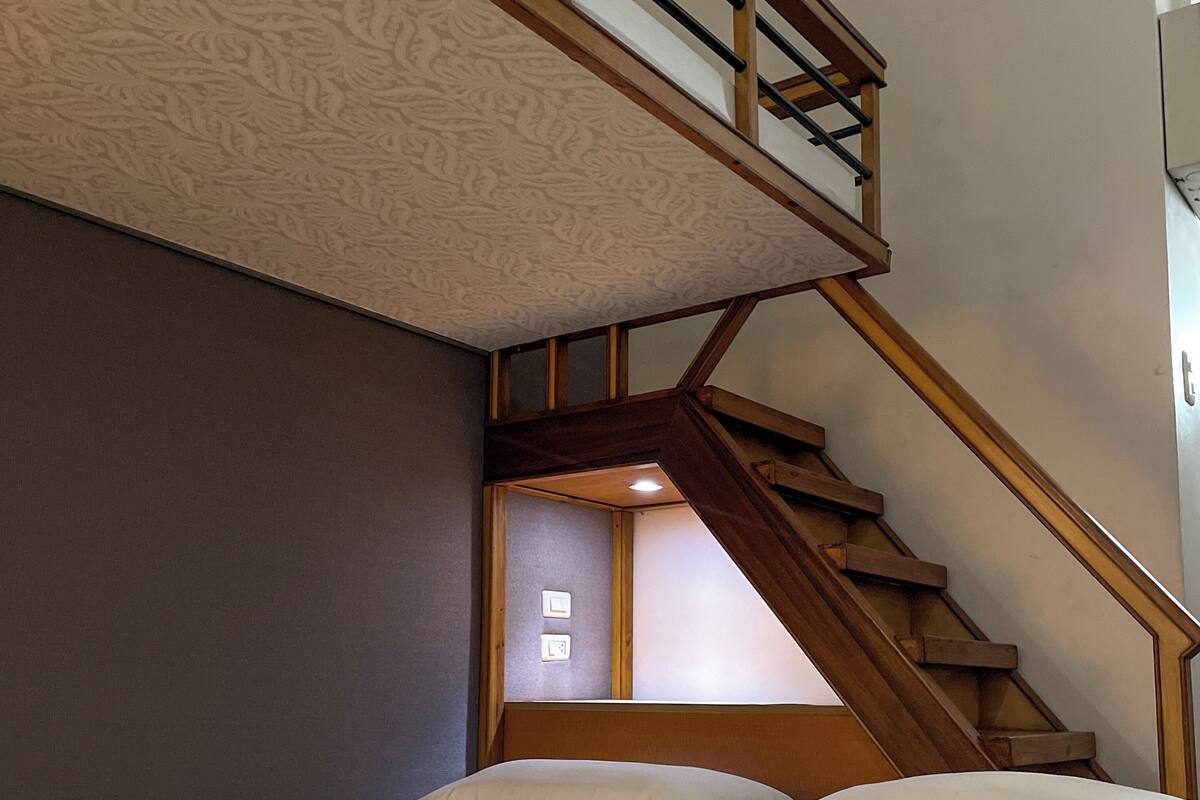 Une chambre à coucher avec un lit, une courtepointe, un escalier et un mur orné d’un motif texturé.