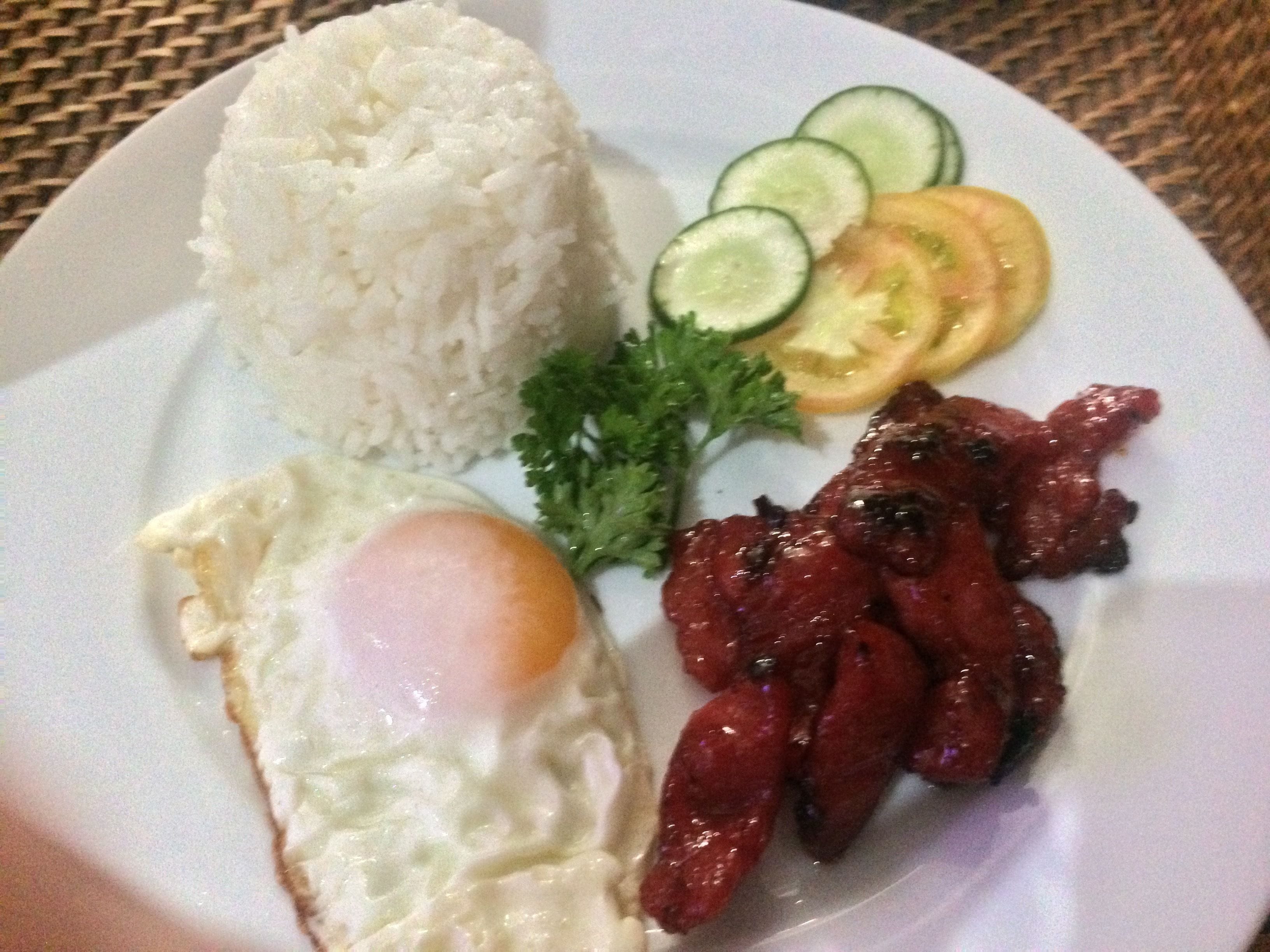 Un plato con arroz blanco, un huevo frito, carne a la parrilla y verduras en rodajas.