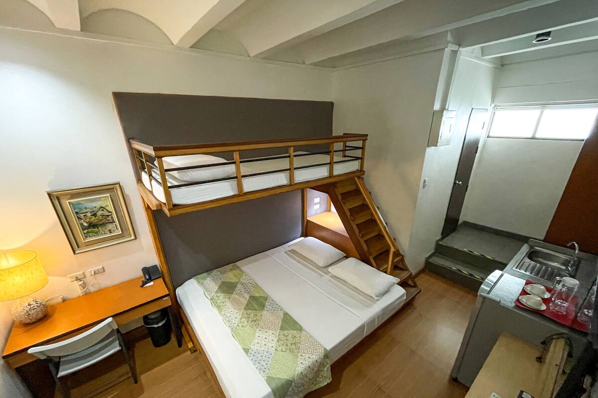 Une chambre avec un lit superposé, un bureau et une kitchenette.
