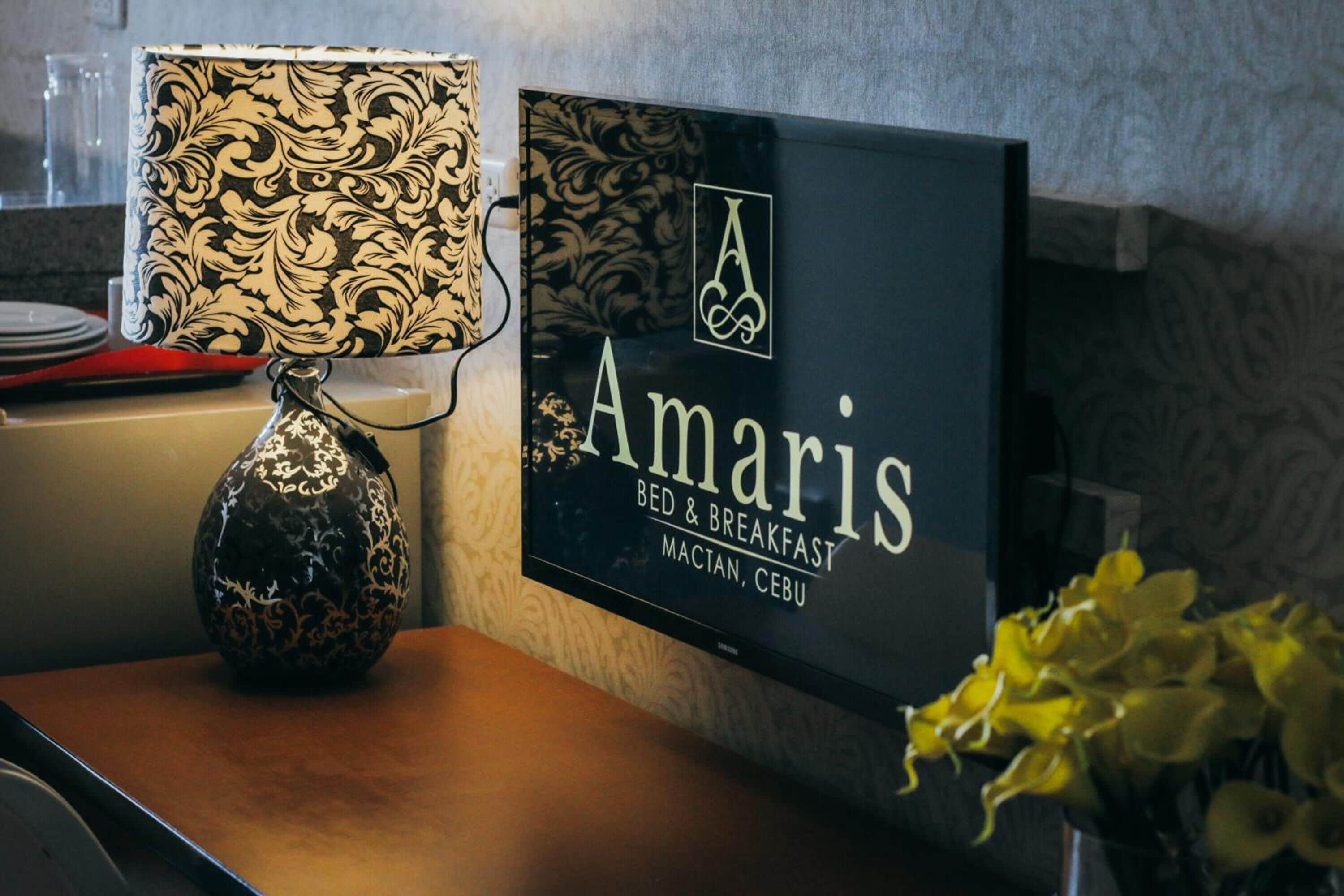 Placa de 'Amaris Bed & Breakfast' com um candeeiro decorativo e um vaso de flores amarelas.