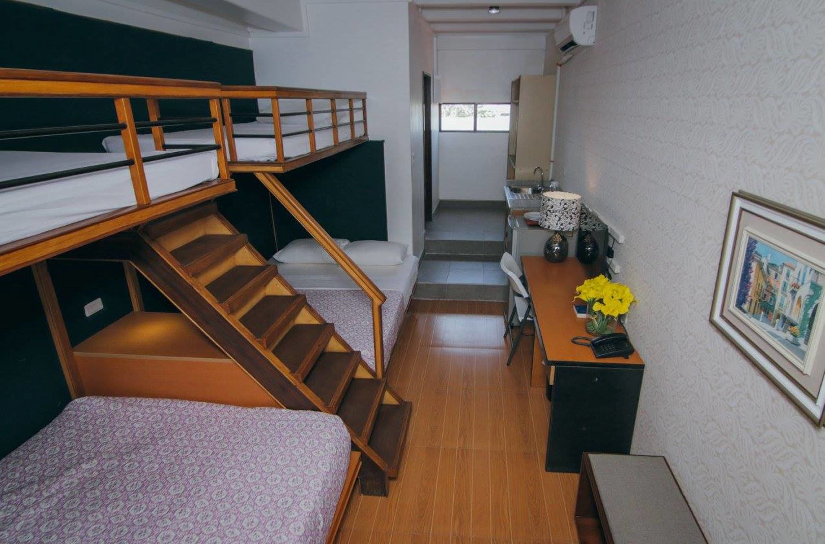 A dormitory room with bunk beds, a staircase, a desk with a telephone, and a small kitchenette.